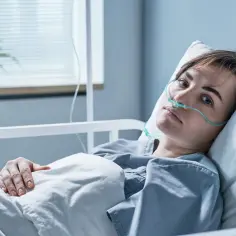 Młoda kobieta w szpitalnym łóżku z tlenoterapią, jej twarz wyraża niepokój. Czy to początek zapalenia opon mózgowych?